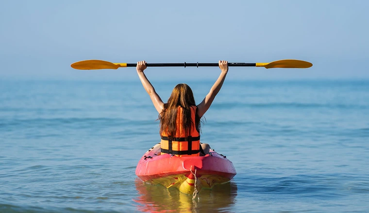 girl holding paddle above her head while kaykaing